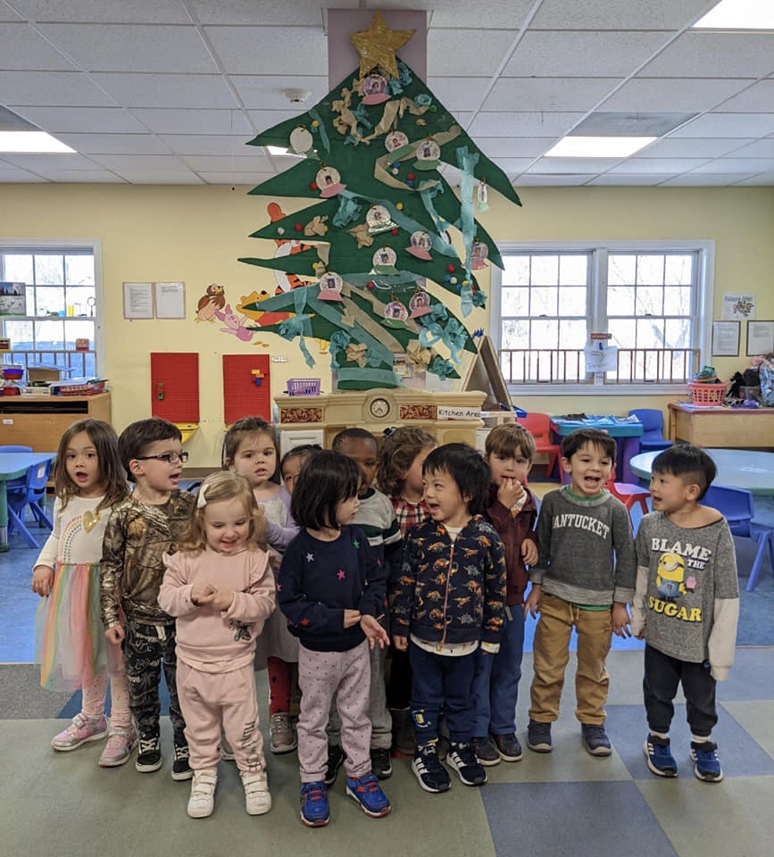 Group of children standing in front of a large paper Christmas tree