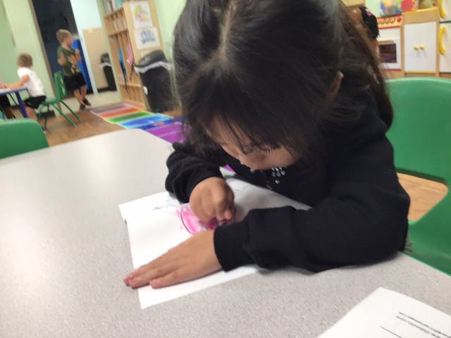 Child drawing on paper at a table in a classroom