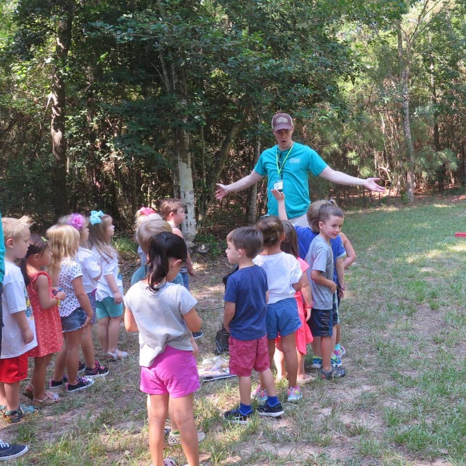 Adult person speaking to a group of children outdoors
