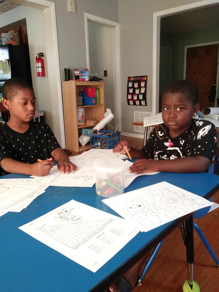Two children sitting at a table with coloring pages and activity sheets