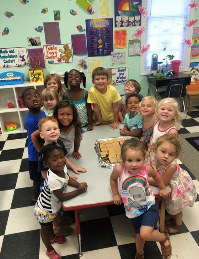 Group of children standing around a table with snacks in a classroom