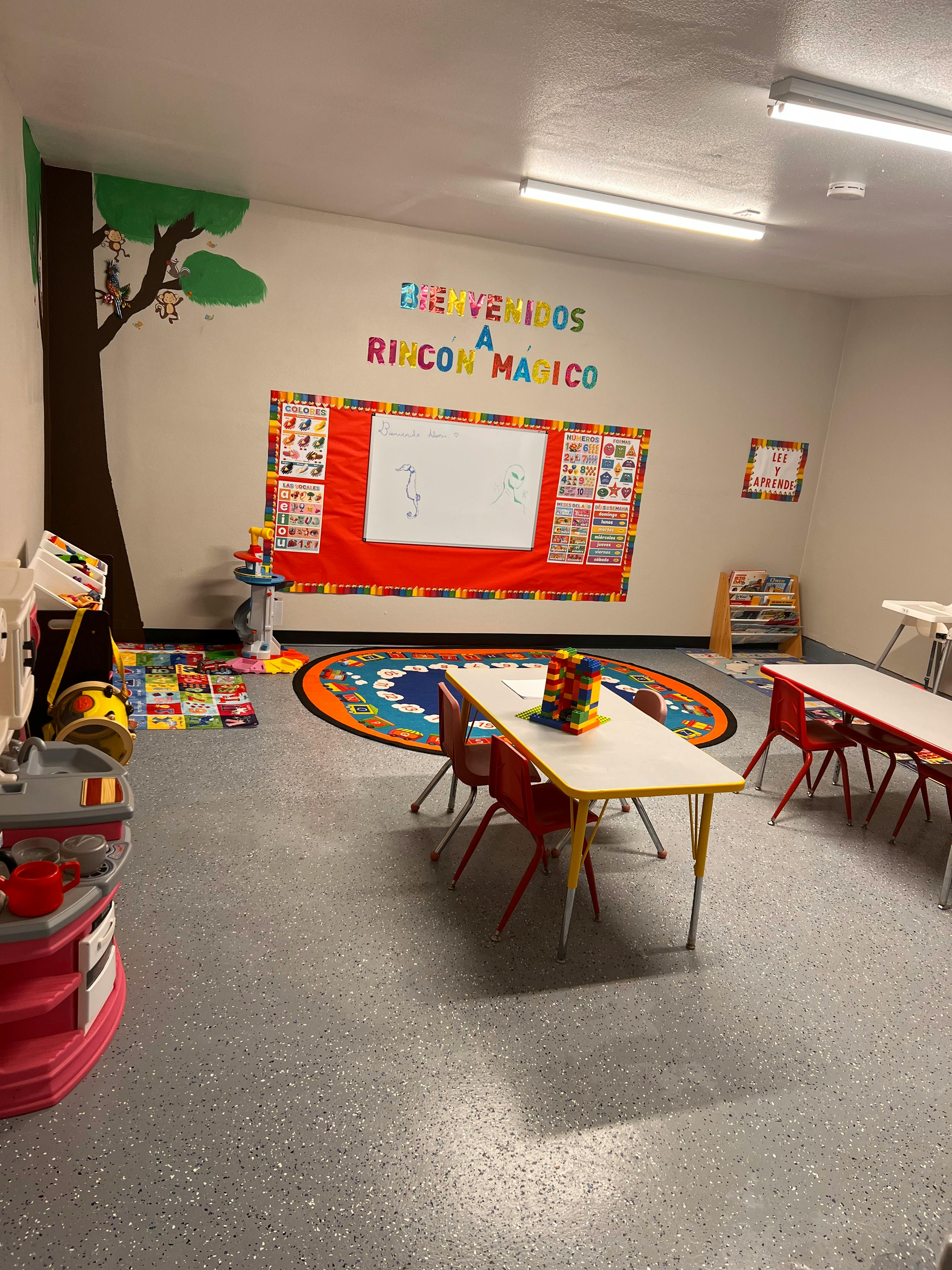 Classroom with small tables and chairs, a whiteboard, and a tree mural