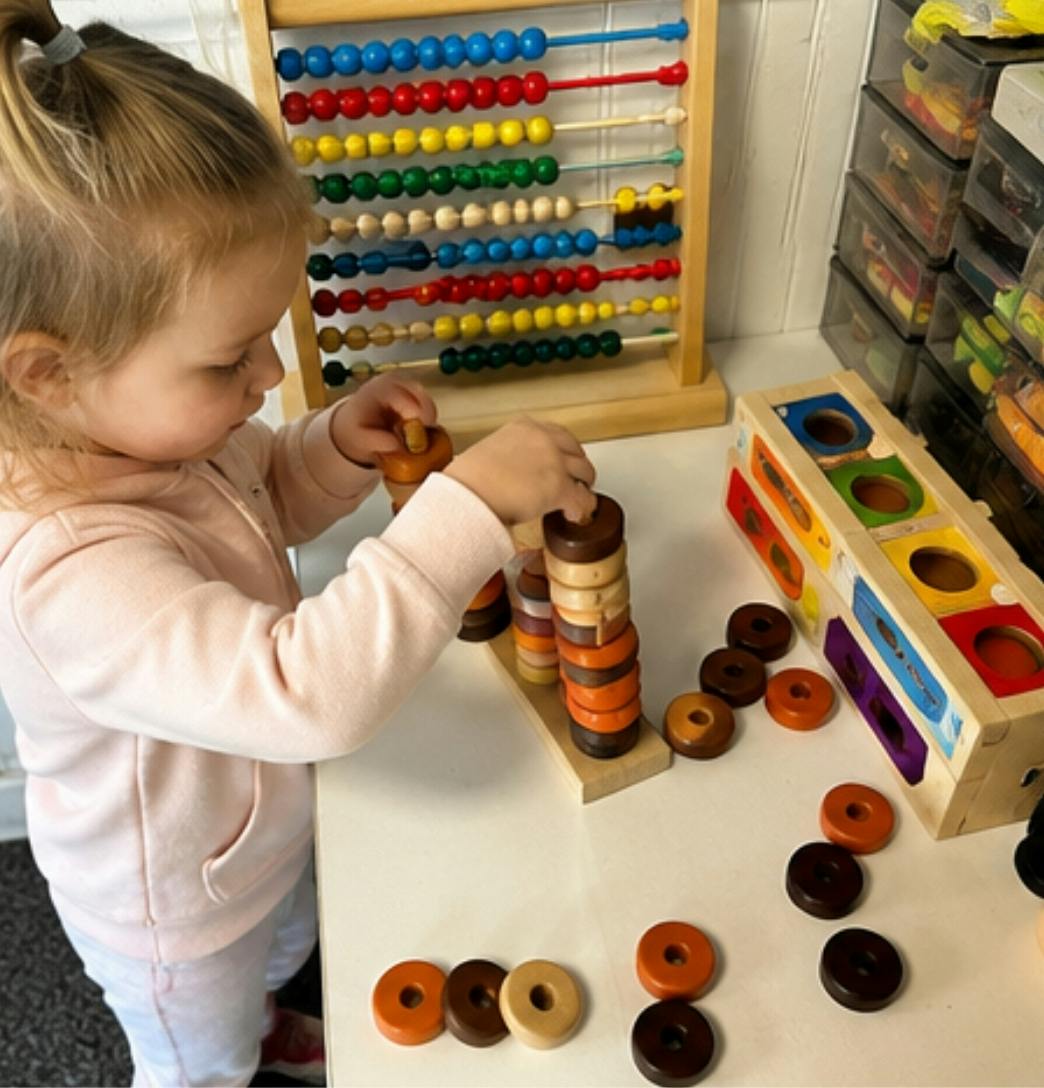 Child playing with a wooden stacking toy at a table with an abacus nearby