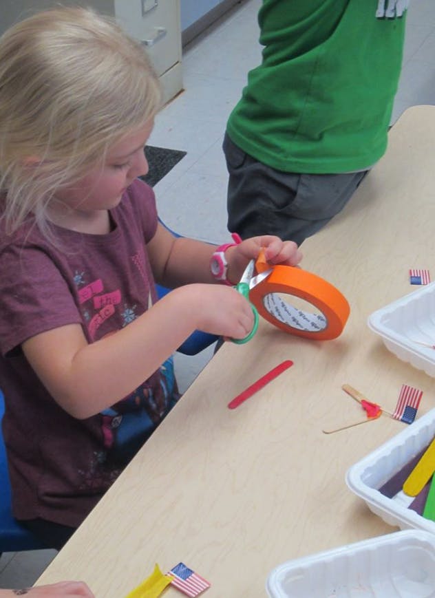 Child cutting orange tape with scissors at a table