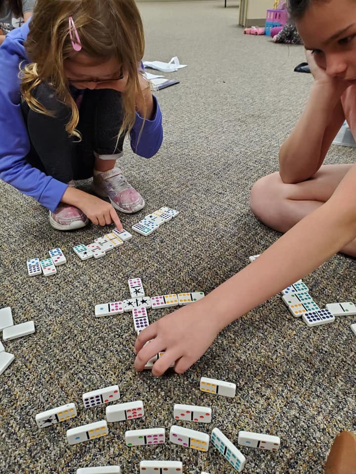 Two children playing dominoes on a carpeted floor