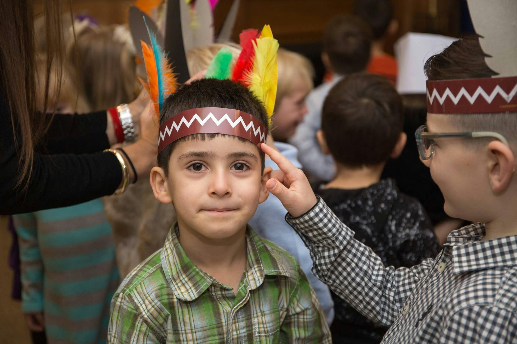 Child in a feathered headband looking forward, another child pointing at right