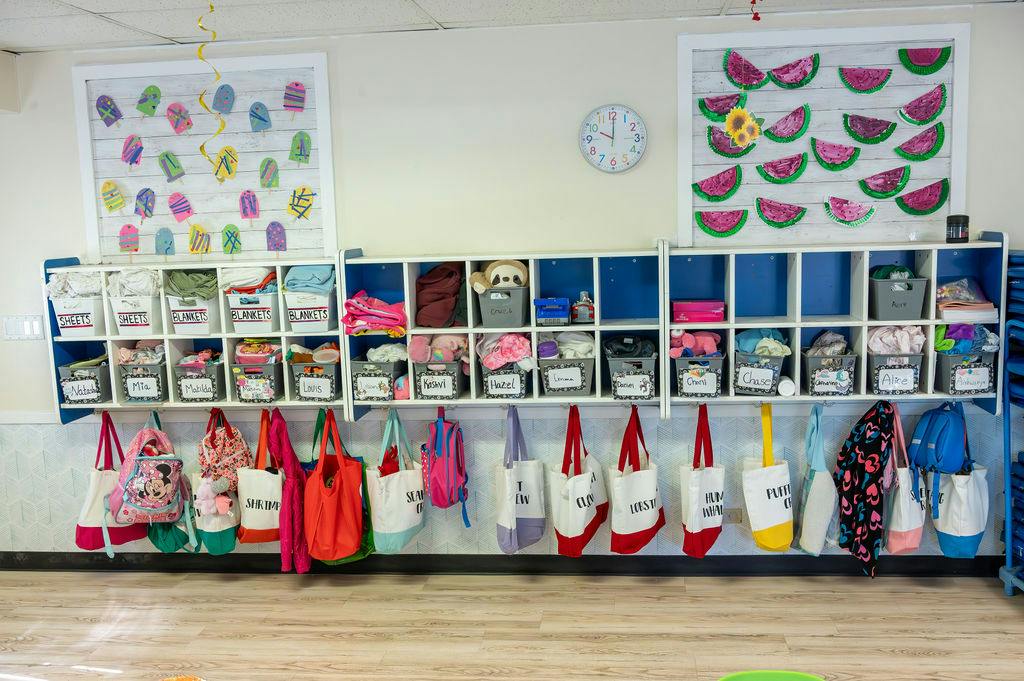 Classroom storage cubbies with labeled bins and colorful bags hanging below