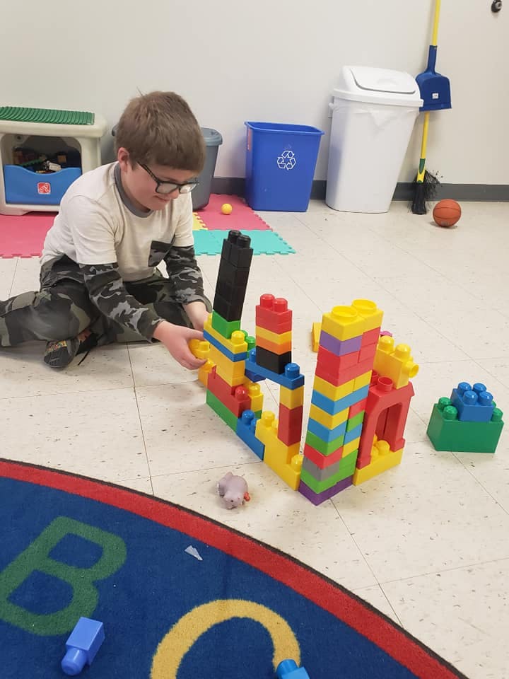 Child in glasses building with colorful blocks on the floor
