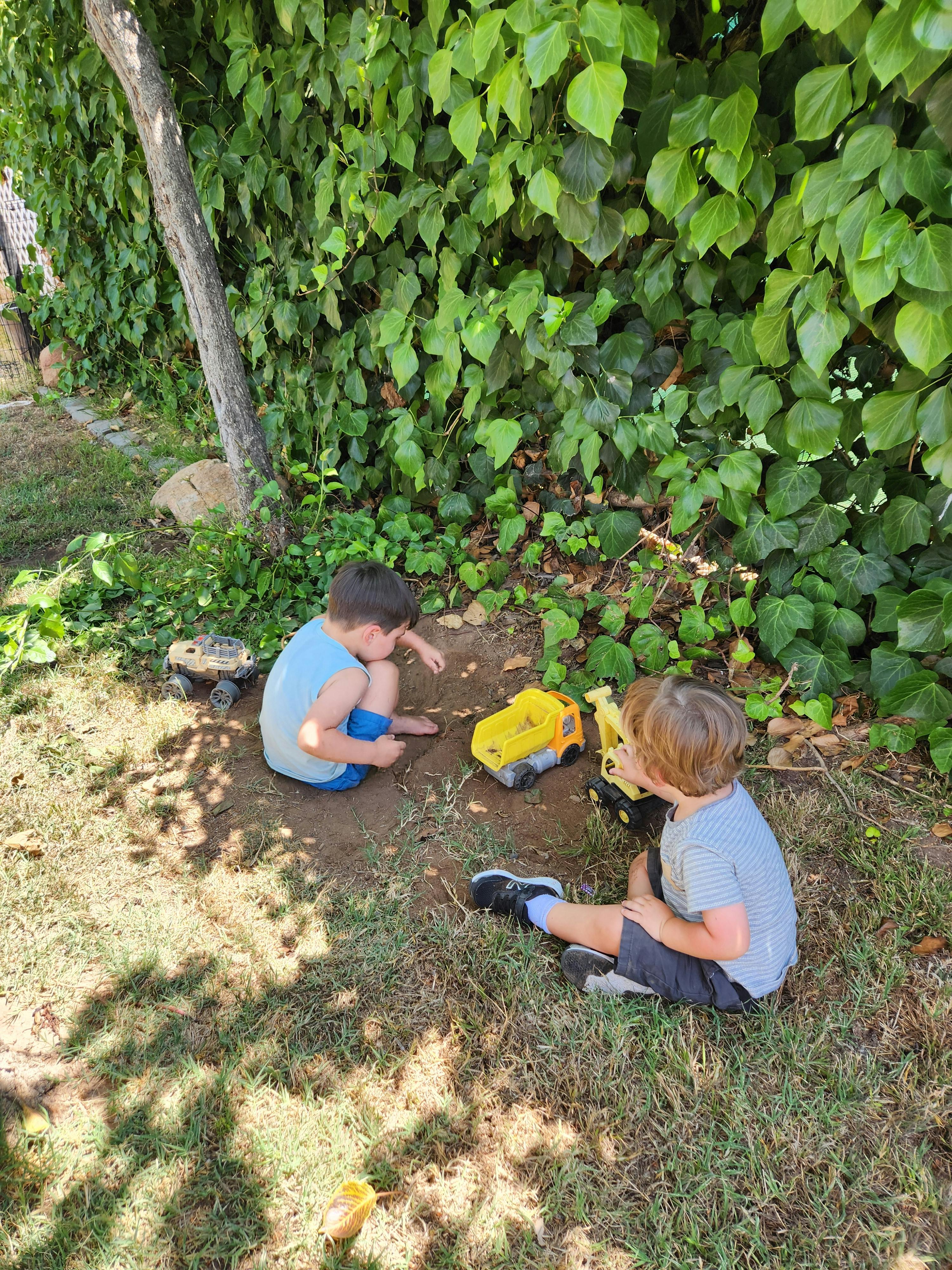 Two children playing with toy trucks in dirt