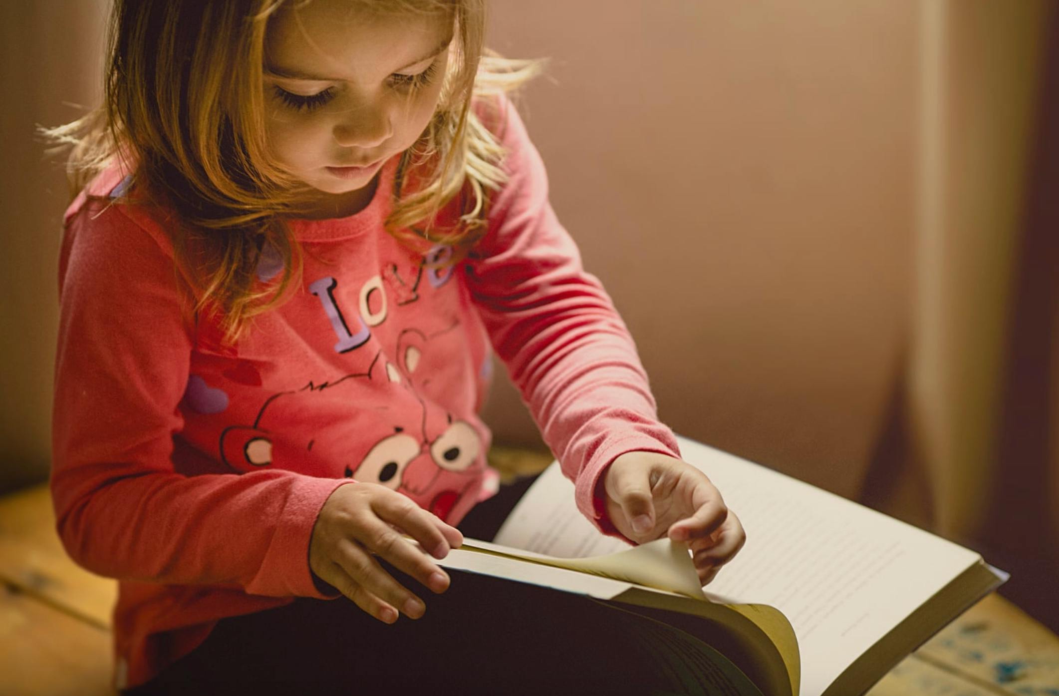 Child looking down at an open book, turning a page
