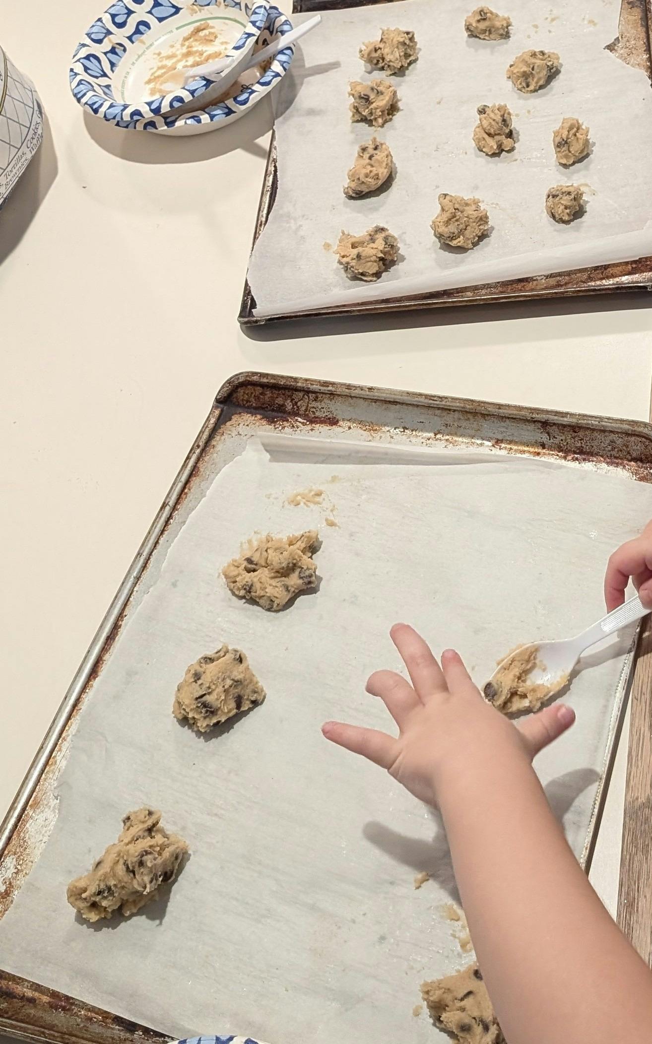 Child's hand scooping cookie dough onto a baking sheet