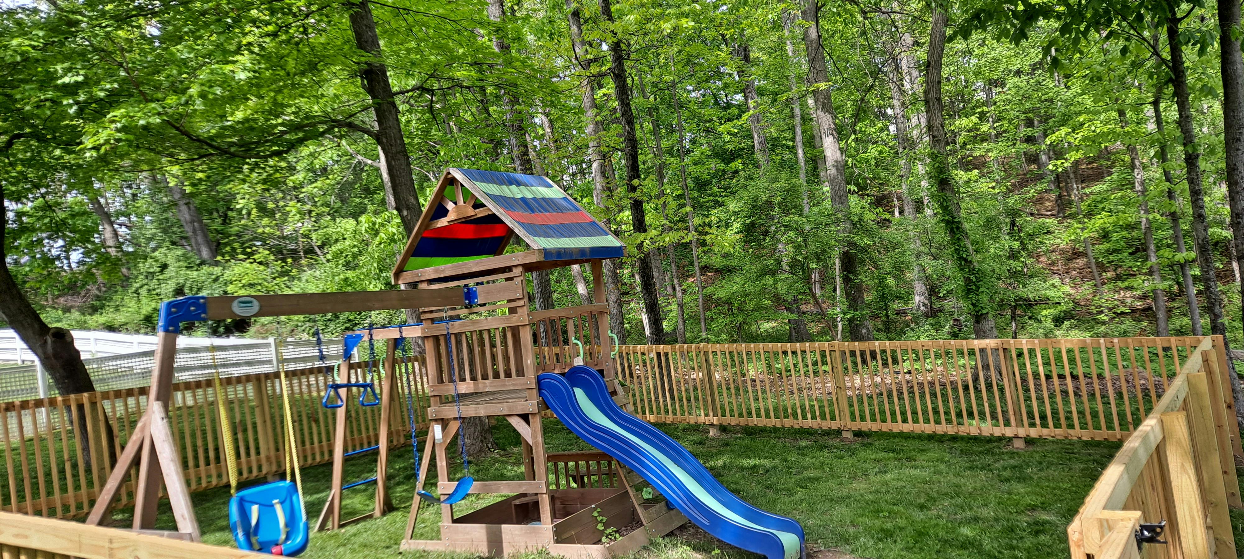 Wooden playground set with a slide and swings in a fenced yard