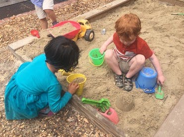 Two children playing in a sandbox with buckets and toys
