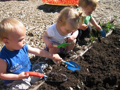 Three children playing in dirt with small shovels