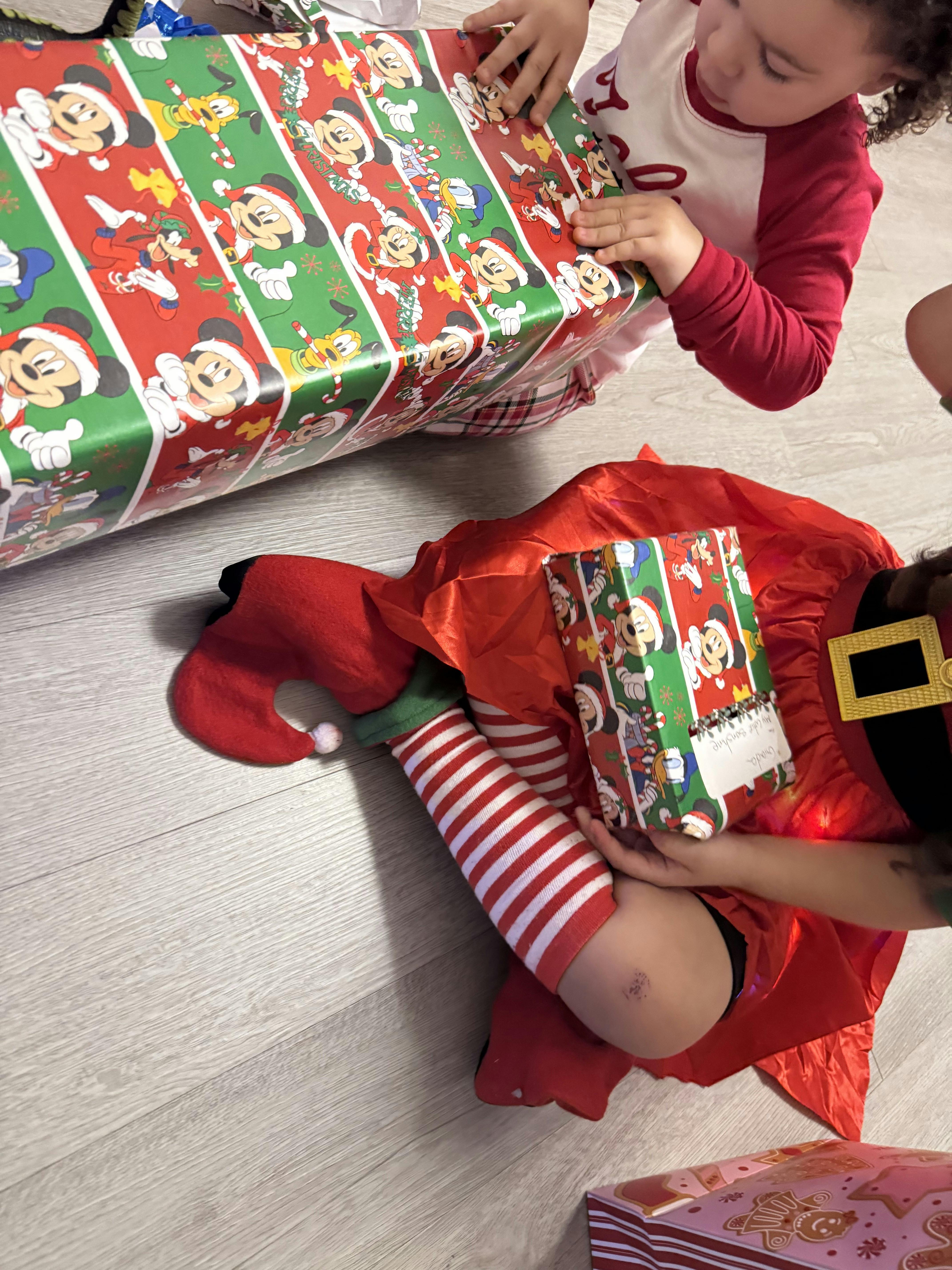 Child in red and white pajamas opening a gift wrapped in Mickey Mouse paper