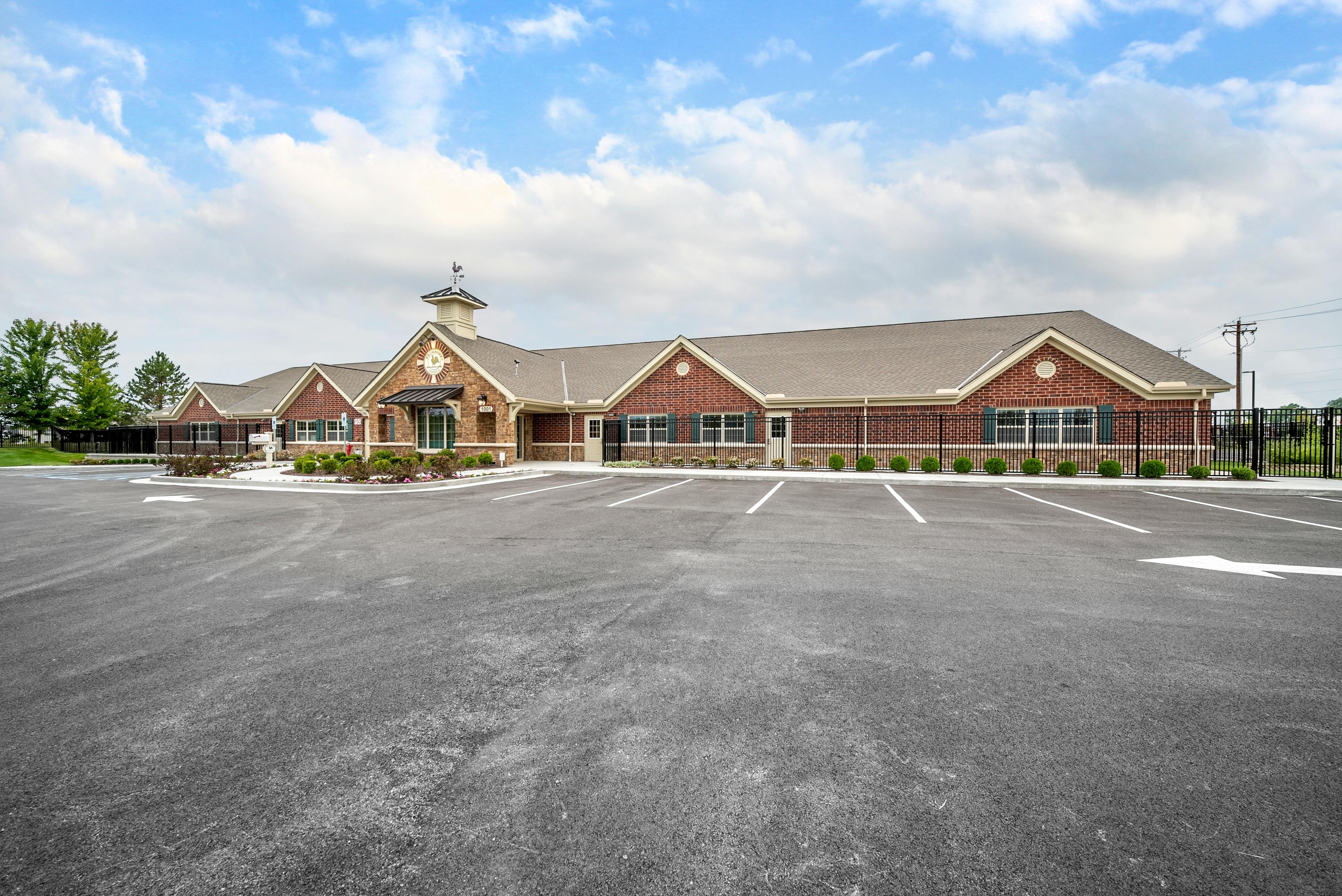 Exterior view of a long brick building with a parking lot in front