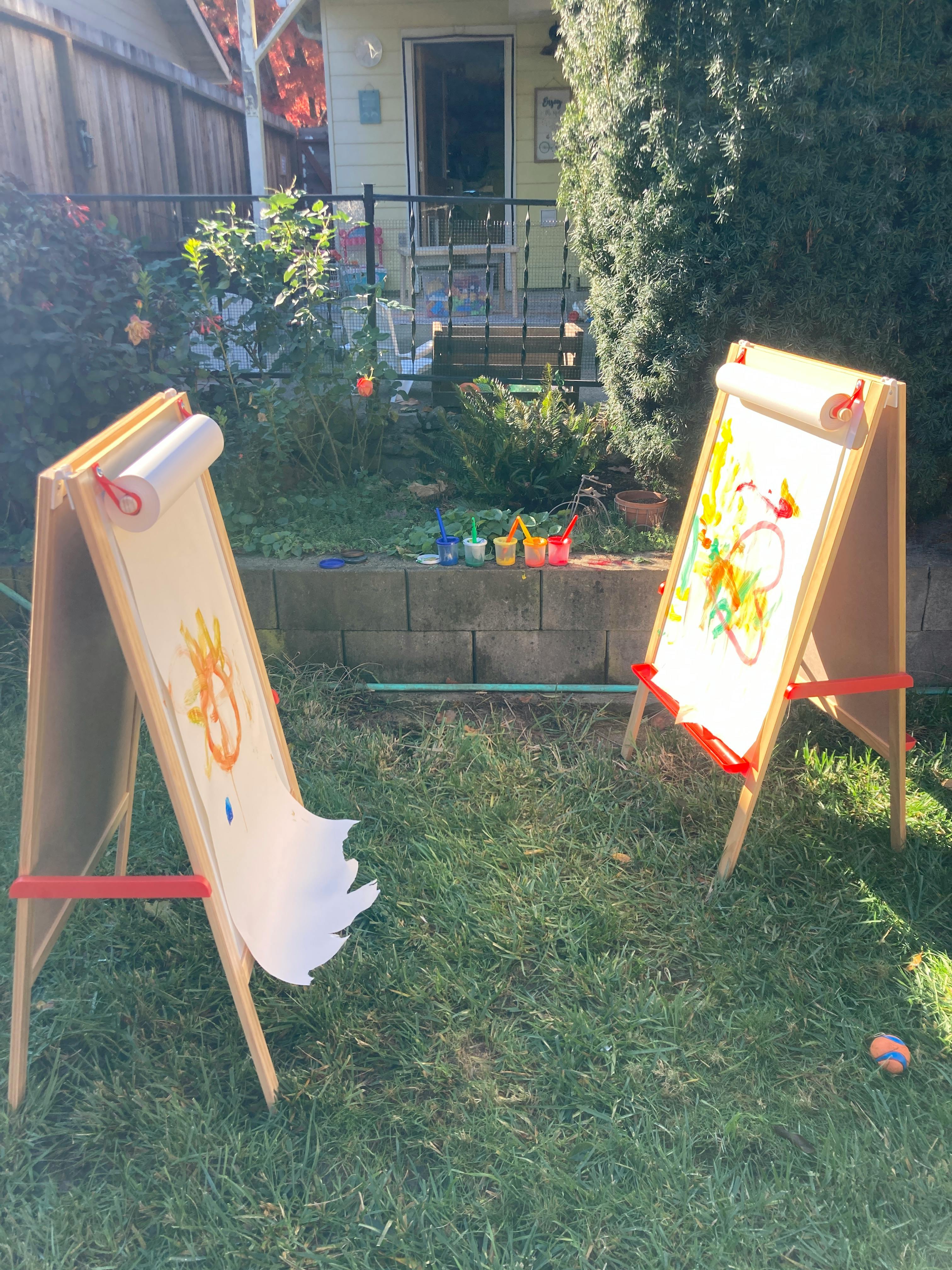 Two easels with paper and colorful drawings on a grassy lawn