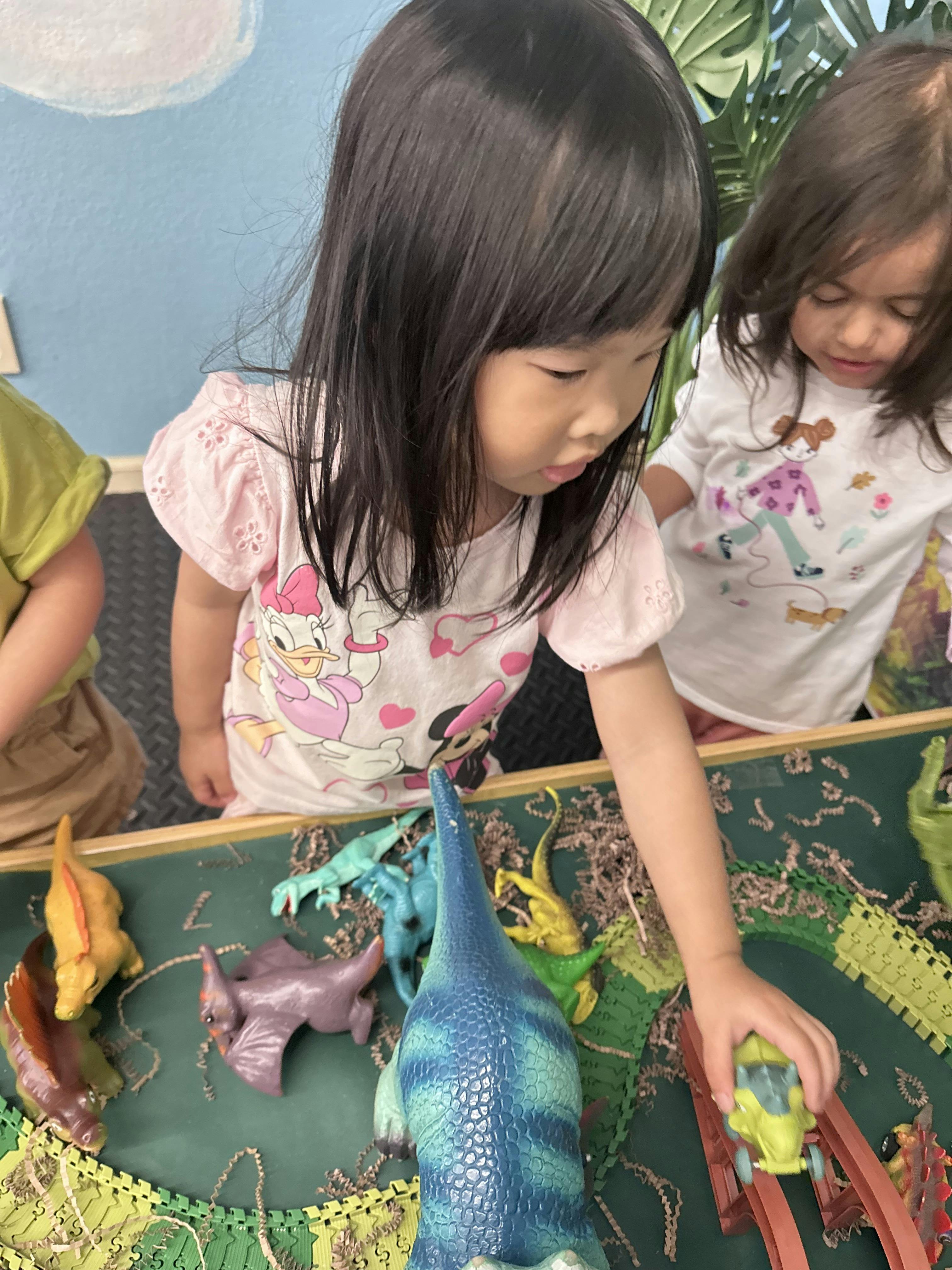 Child playing with toy dinosaurs and a car on a playmat