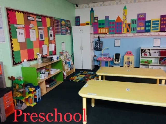 Preschool classroom with colorful bulletin board and yellow tables