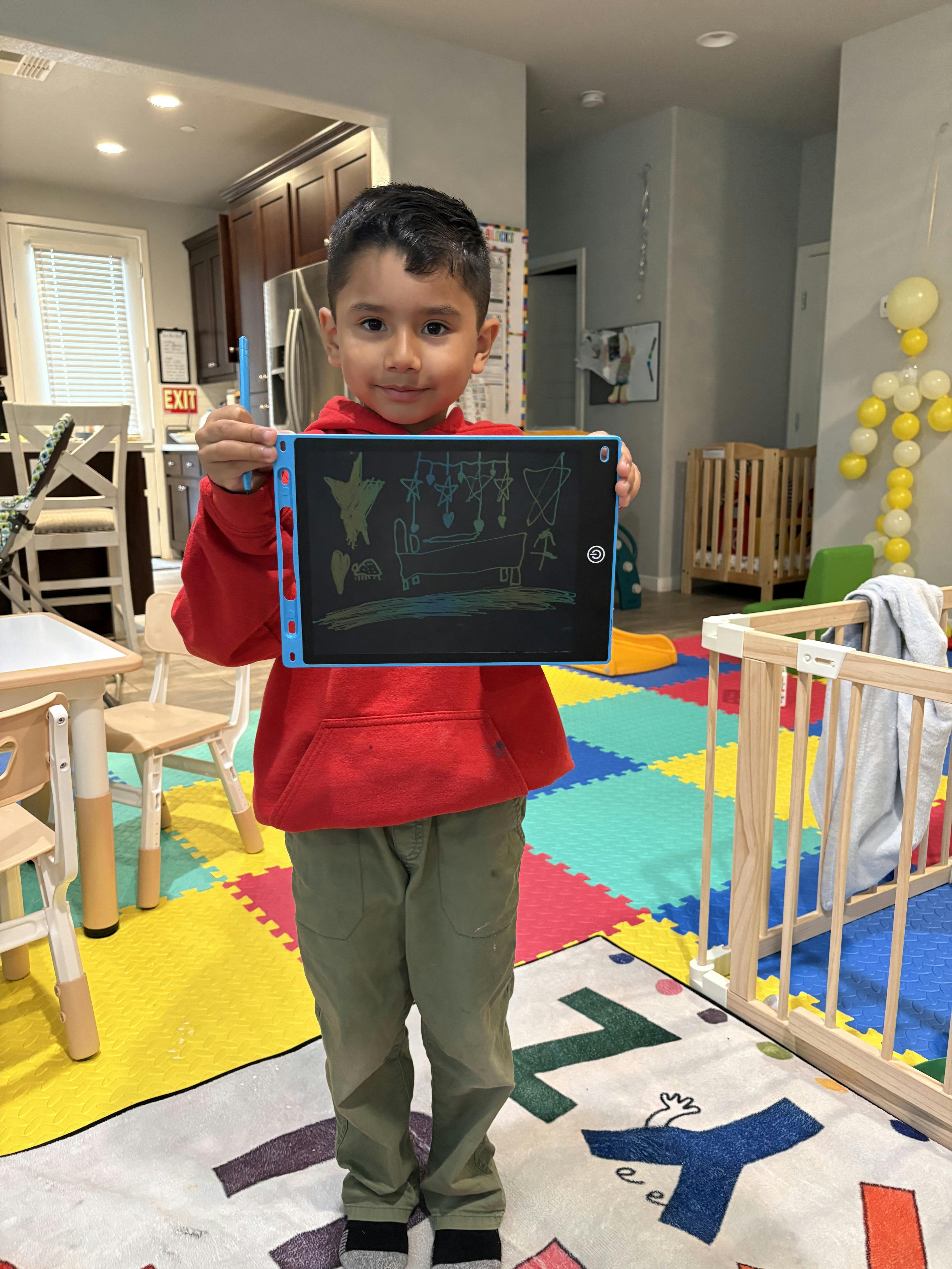 Child in a red hoodie holding up a blue drawing tablet with a drawing on it