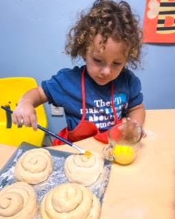 Child brushing liquid onto pastries on a baking sheet