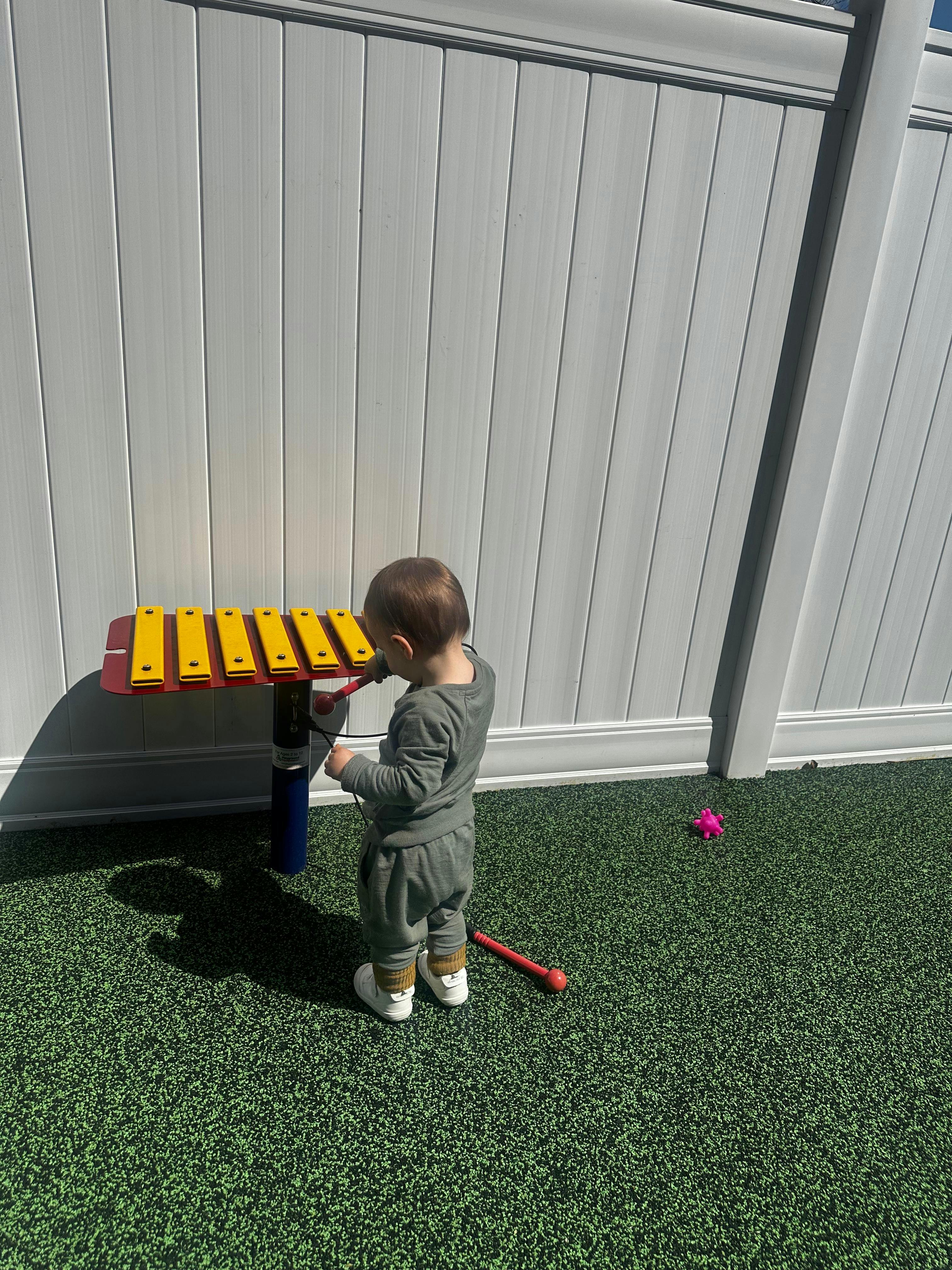Child playing a large yellow and red xylophone outdoors