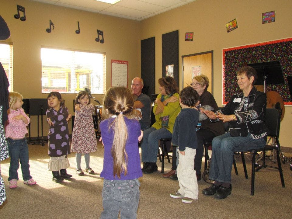 Children standing in a circle with adults seated in a room