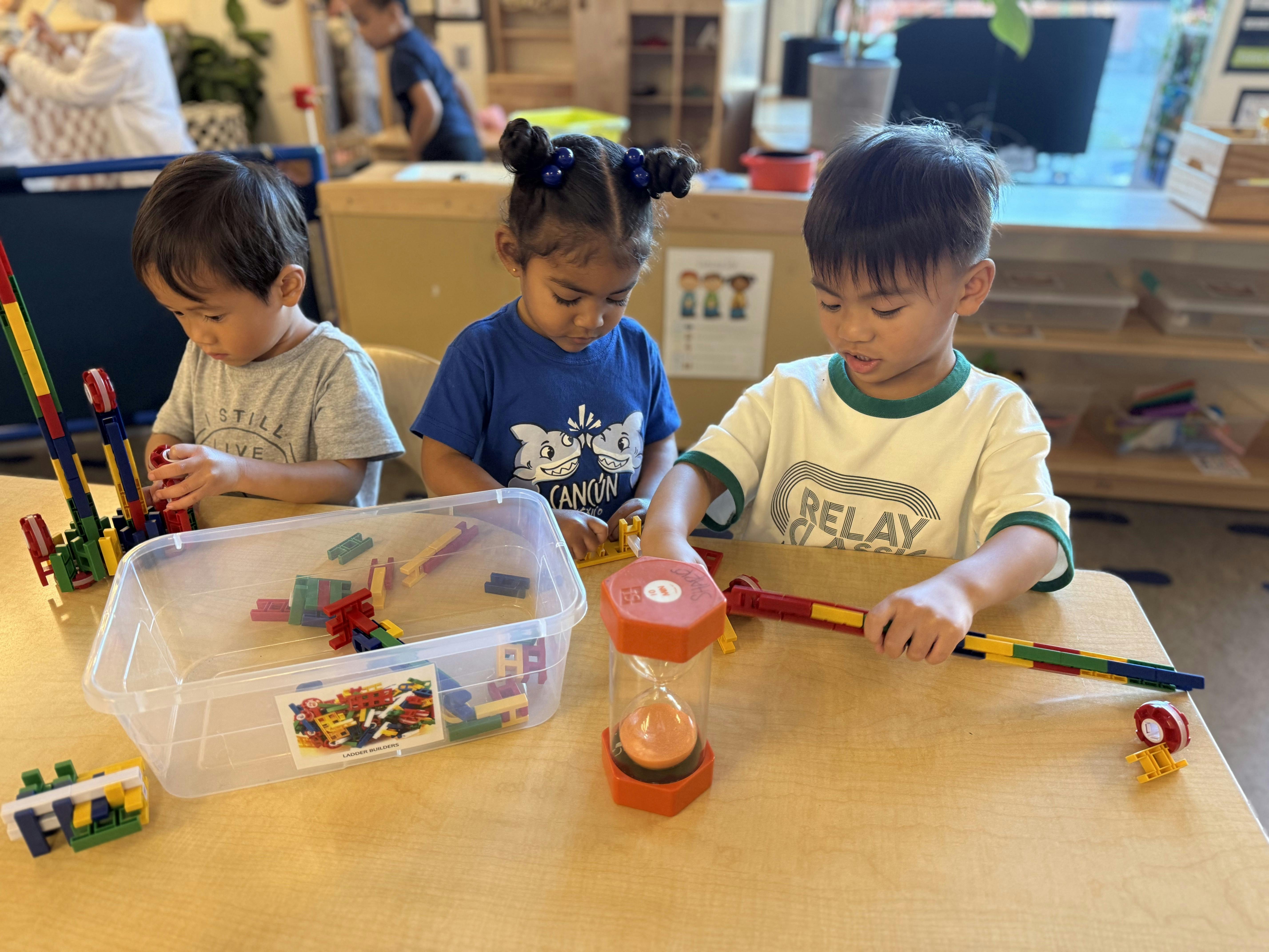 Three children sitting at a table playing with building blocks