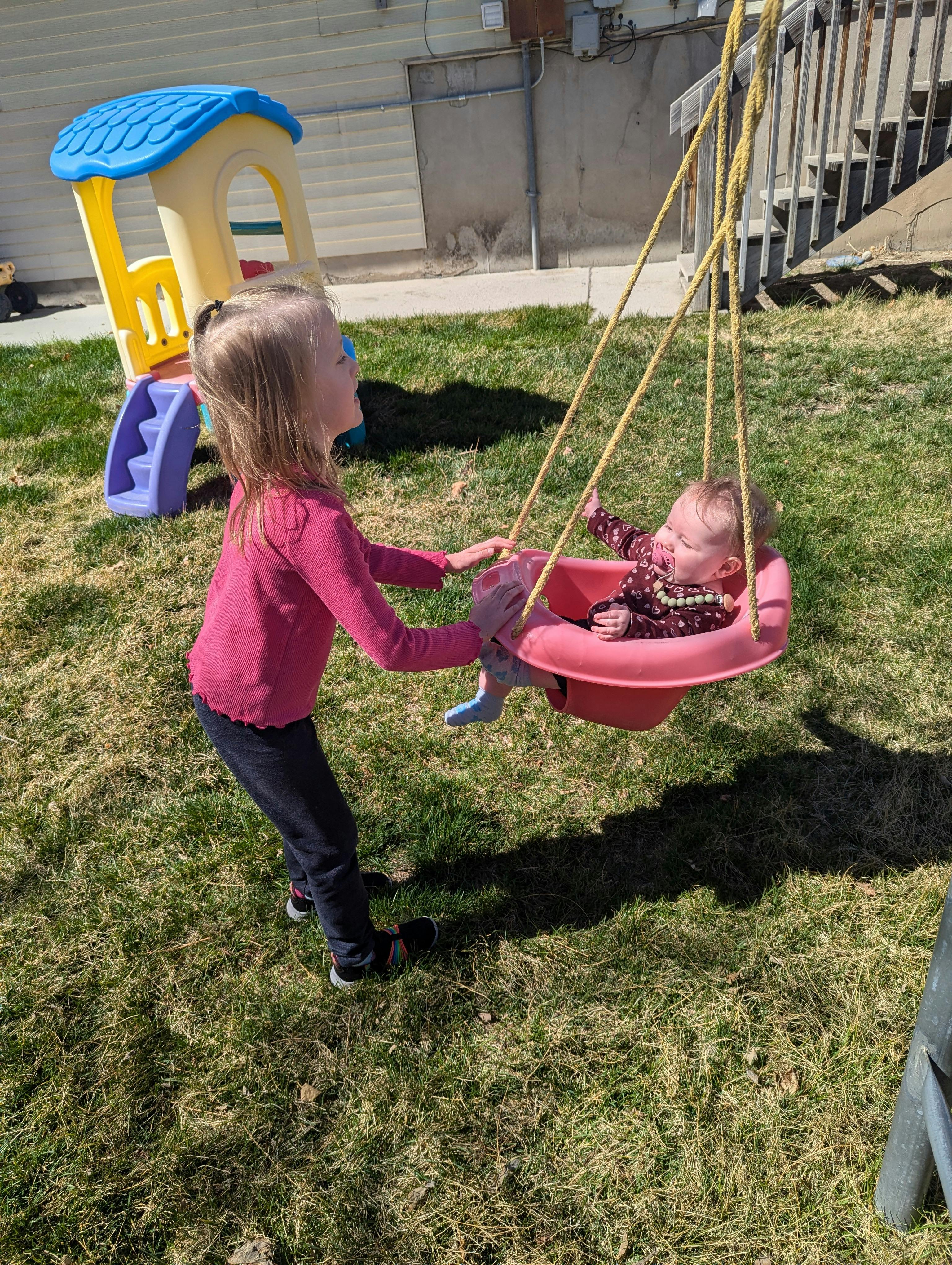 Child pushing a baby in a swing outdoors
