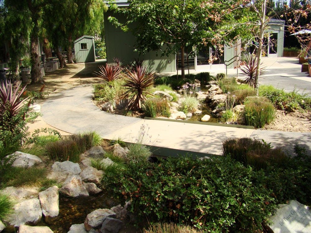 Curved path through a garden with small stream and green buildings