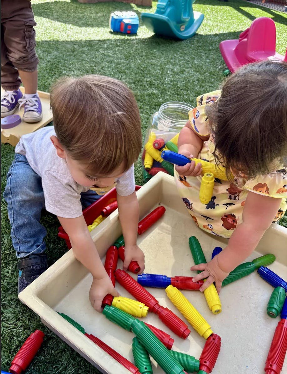 Two children playing with colorful plastic tubes in a tray