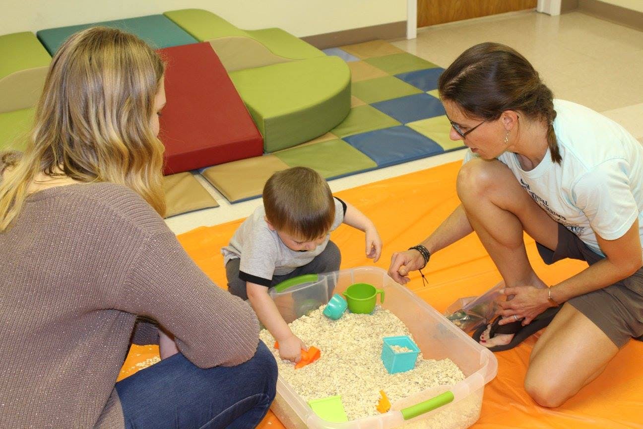Two people and a child playing with sensory bin in a classroom