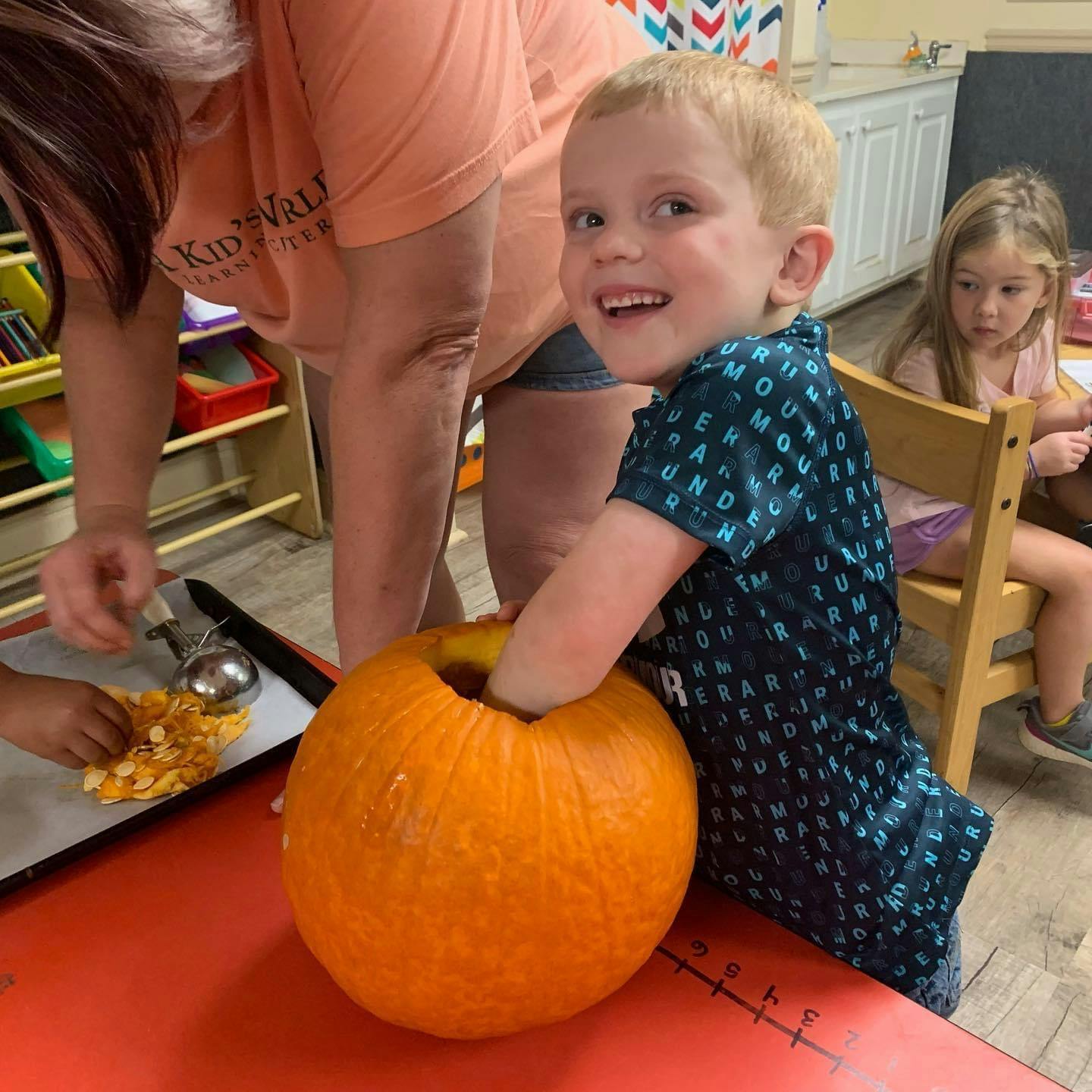 Child with hand inside a pumpkin, another child and adult nearby