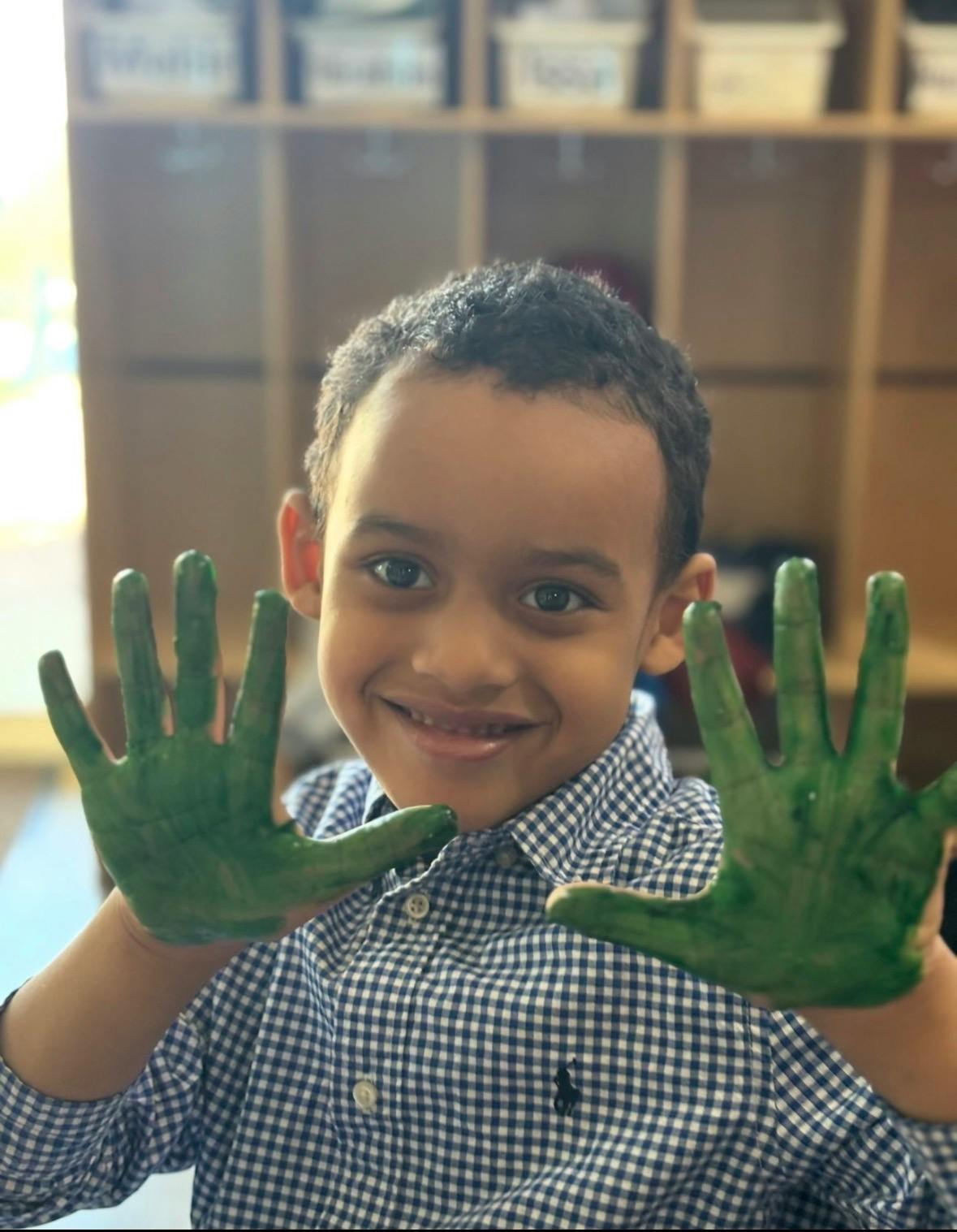 Child showing hands covered in green paint