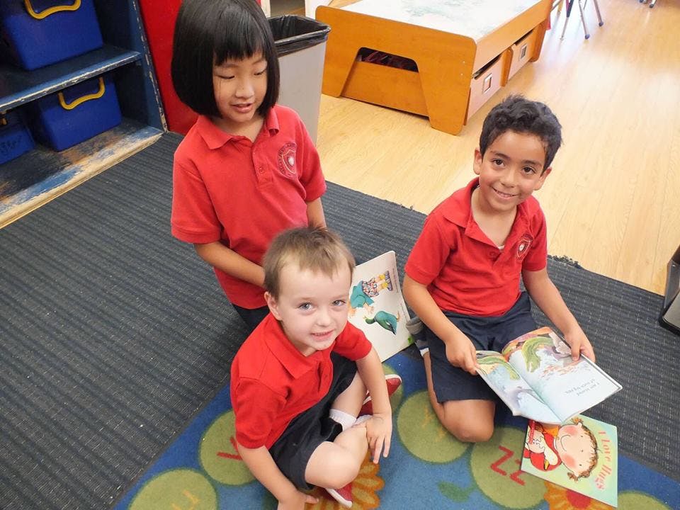 Three children in red shirts looking at books on the floor