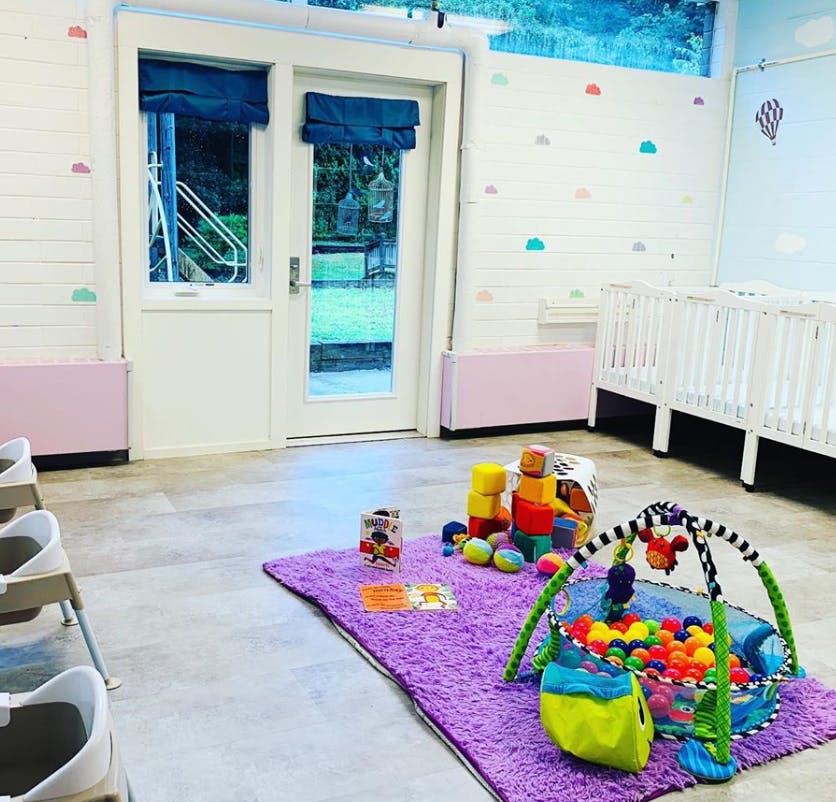 Playroom with a purple rug, toys, and two cribs