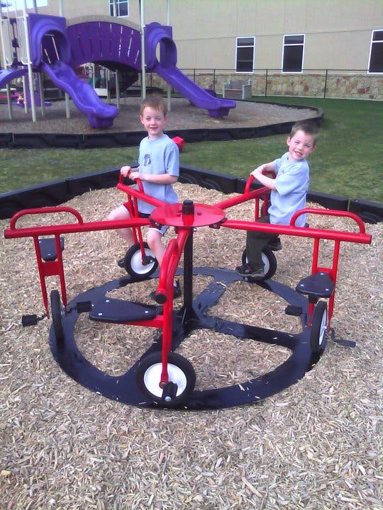 Two children on a red merry-go-round in a playground