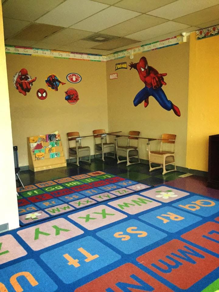 Classroom with Spider-Man wall decals, desks, and an alphabet rug