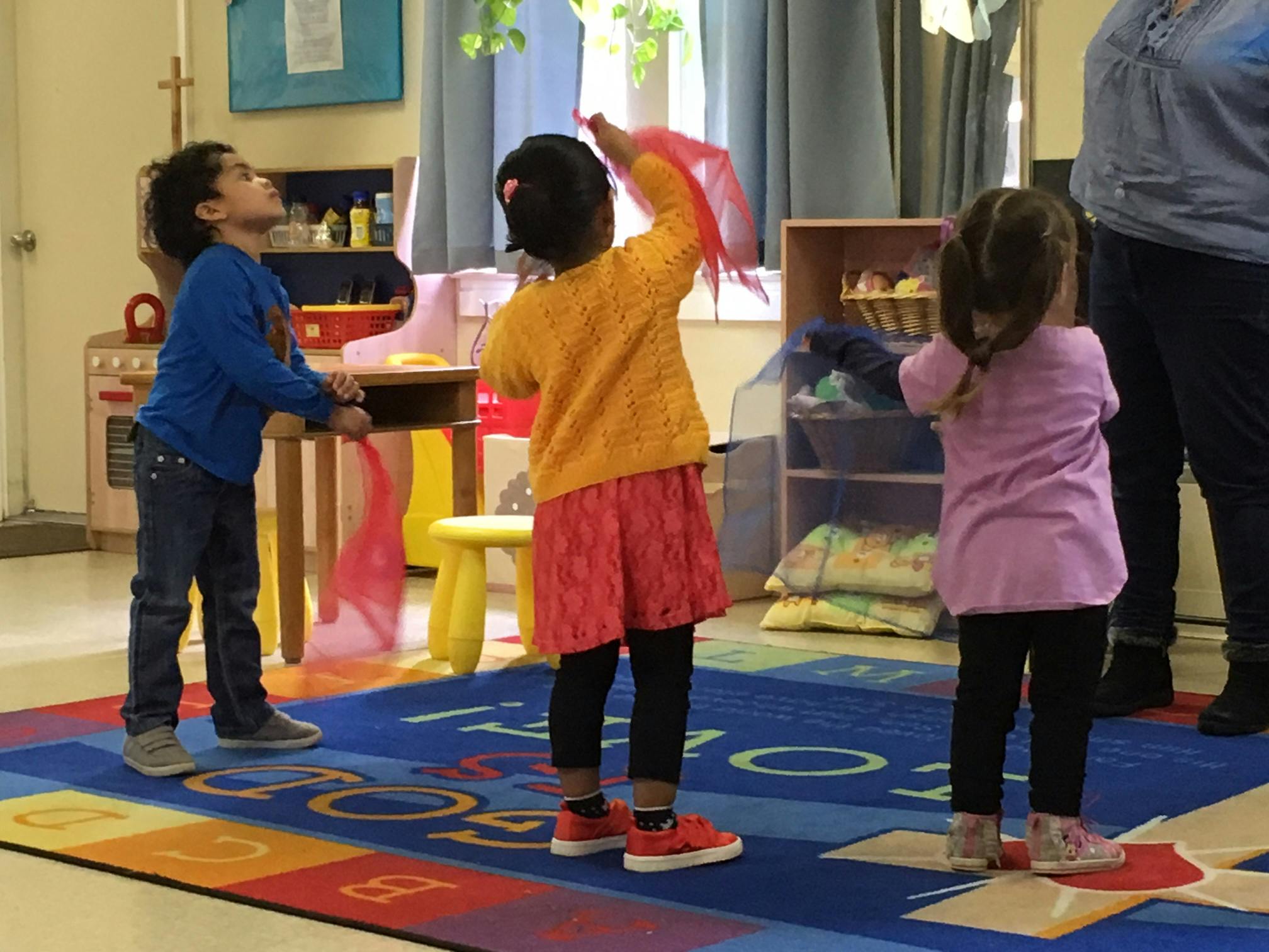 Three children standing on a colorful rug in a classroom