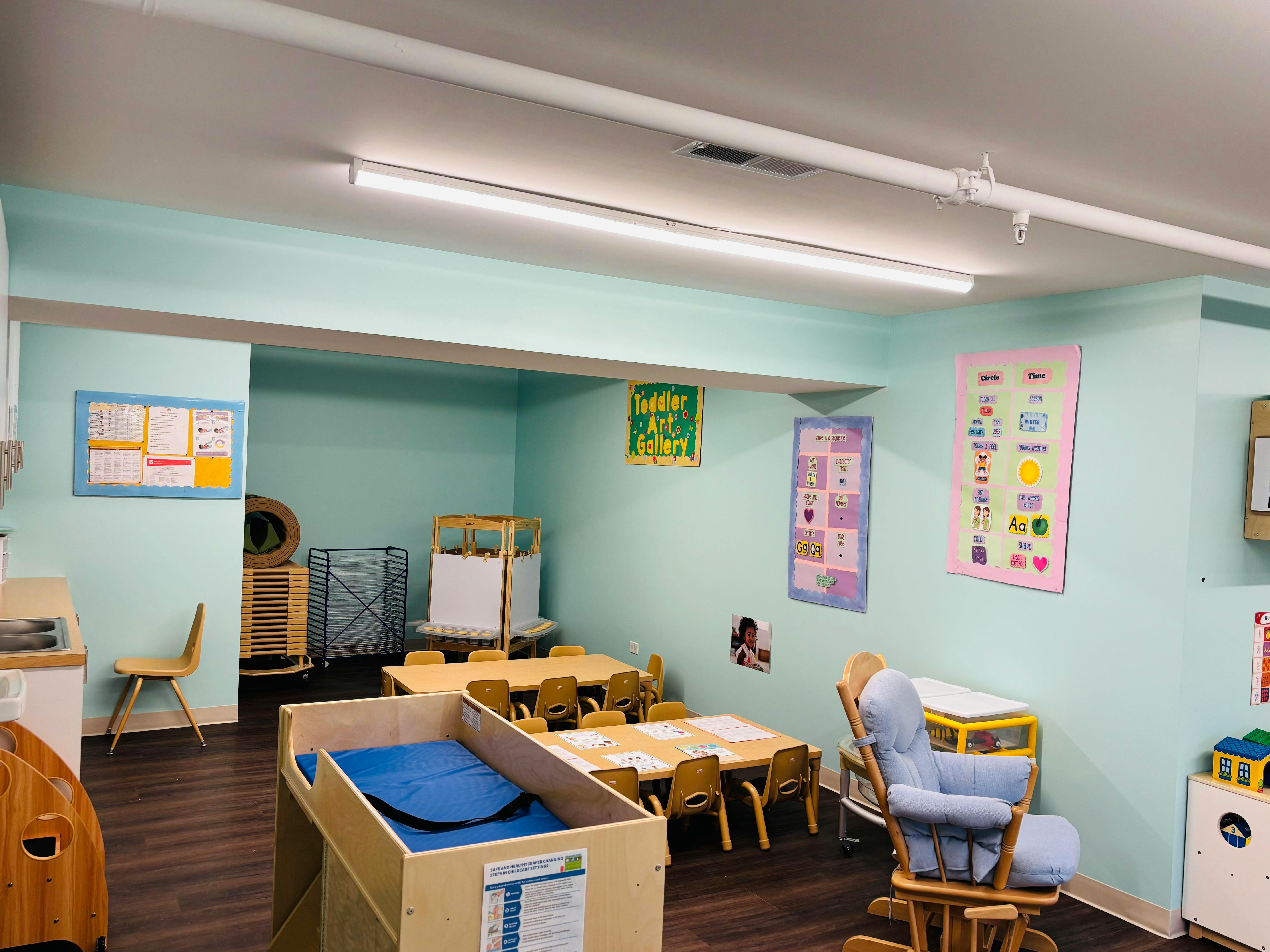 Classroom with small tables and chairs, a crib, and posters on the wall