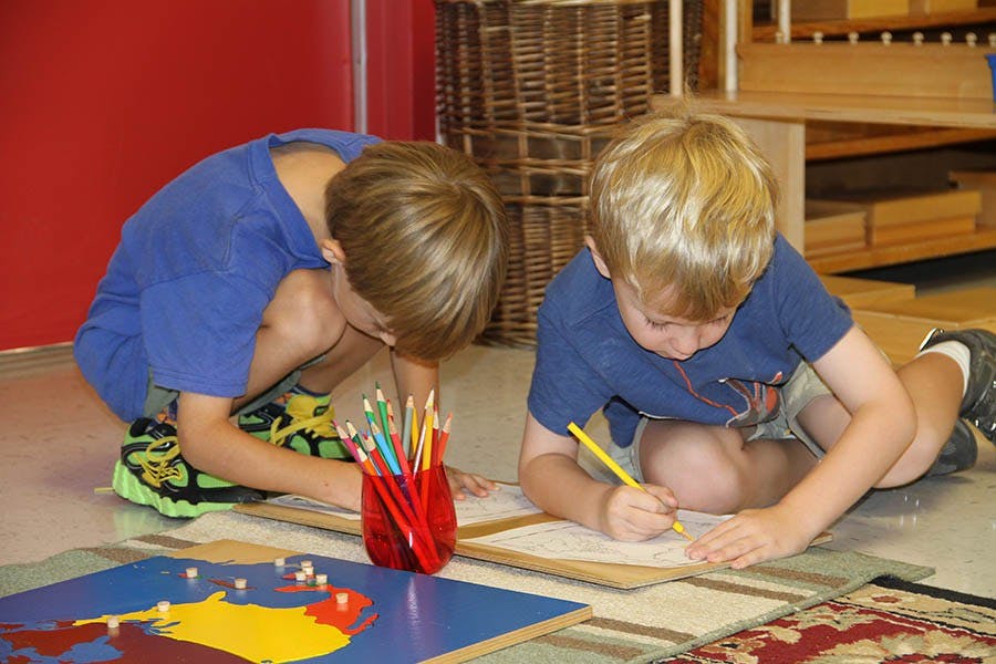 Two children drawing on the floor with colored pencils