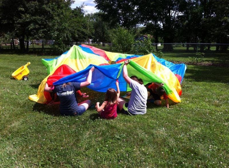 People and children playing with a colorful parachute on grass