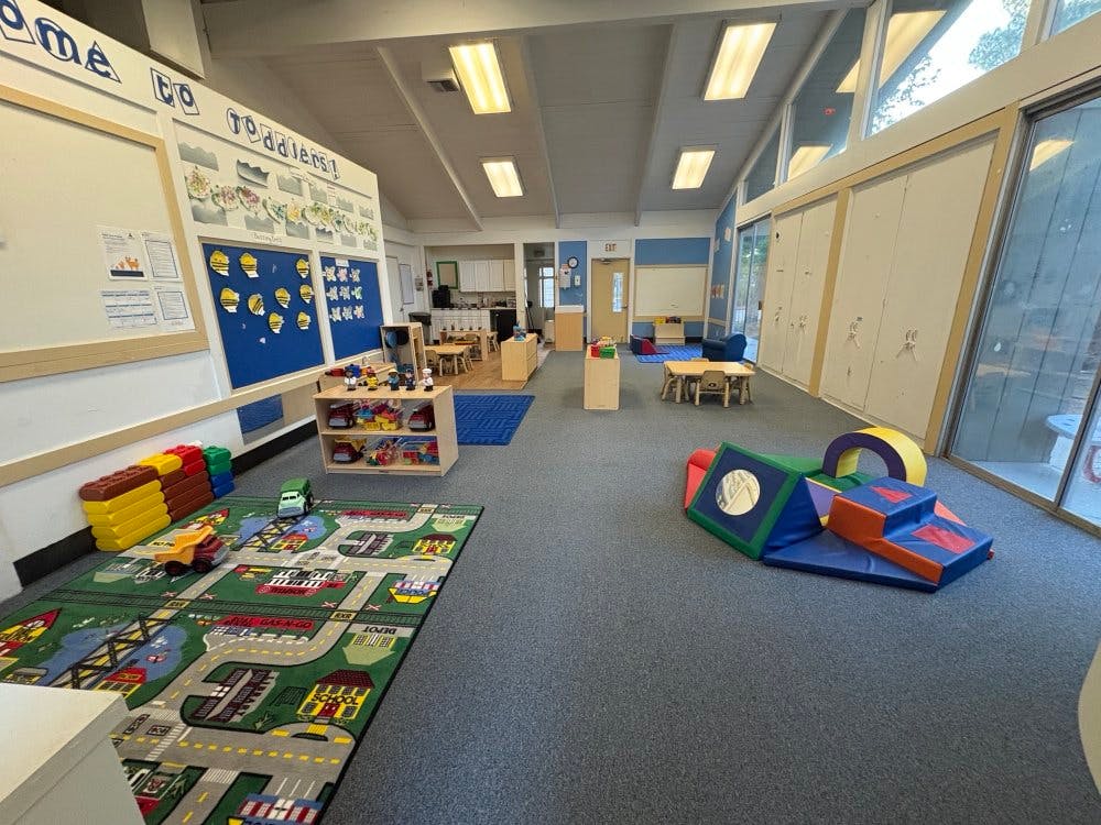 A colorful toddler classroom with various toys, play mats, and learning displays