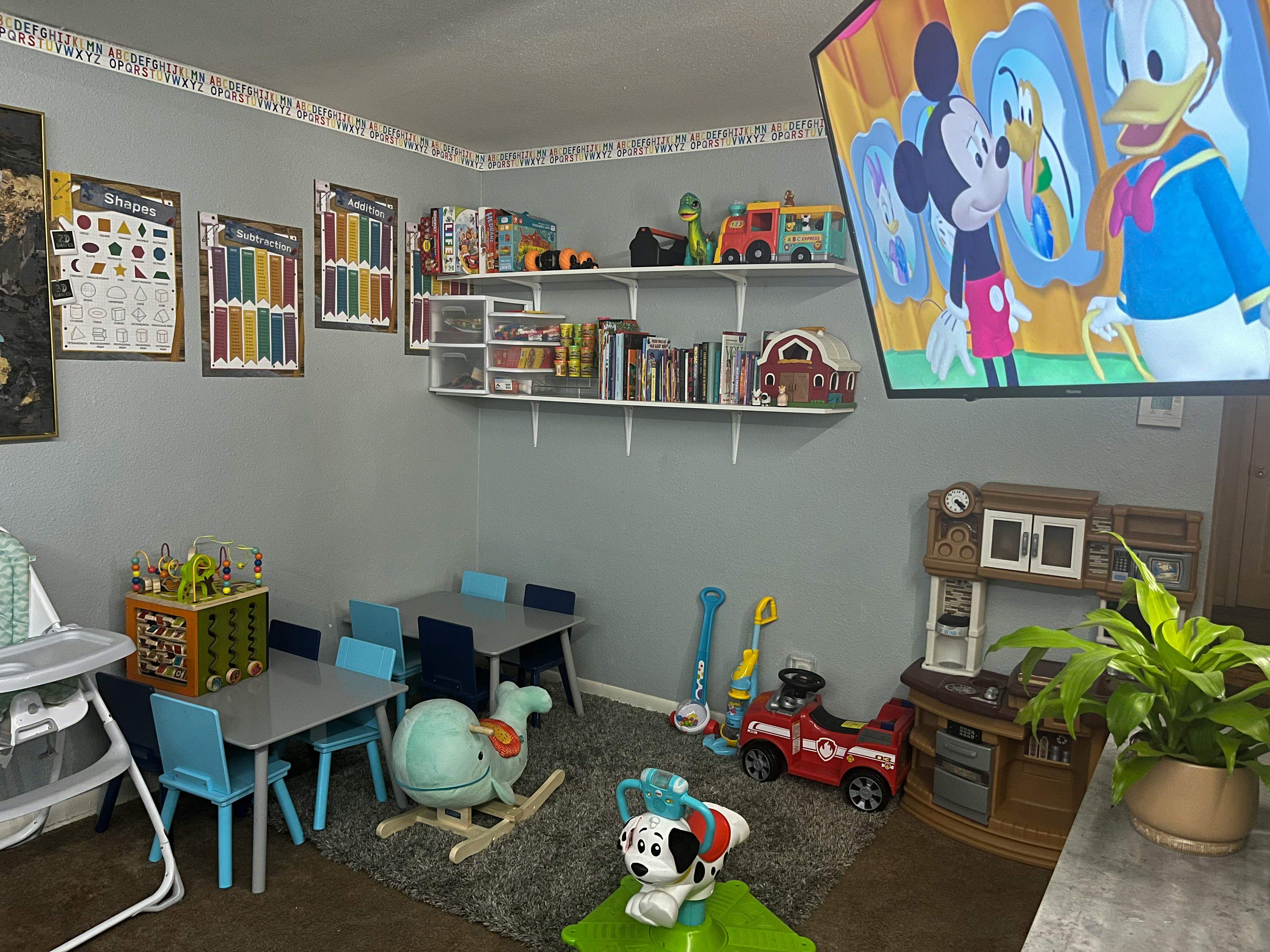 Playroom with small tables and chairs, toys on the floor, and a TV showing cartoons