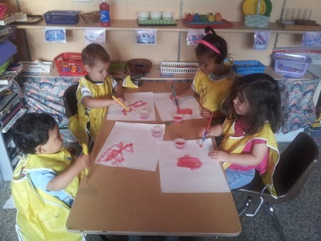 Four children painting at a table in a classroom