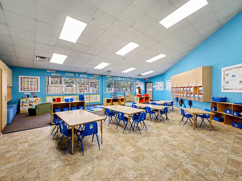 Empty classroom with blue walls, tables, chairs, and cubbies