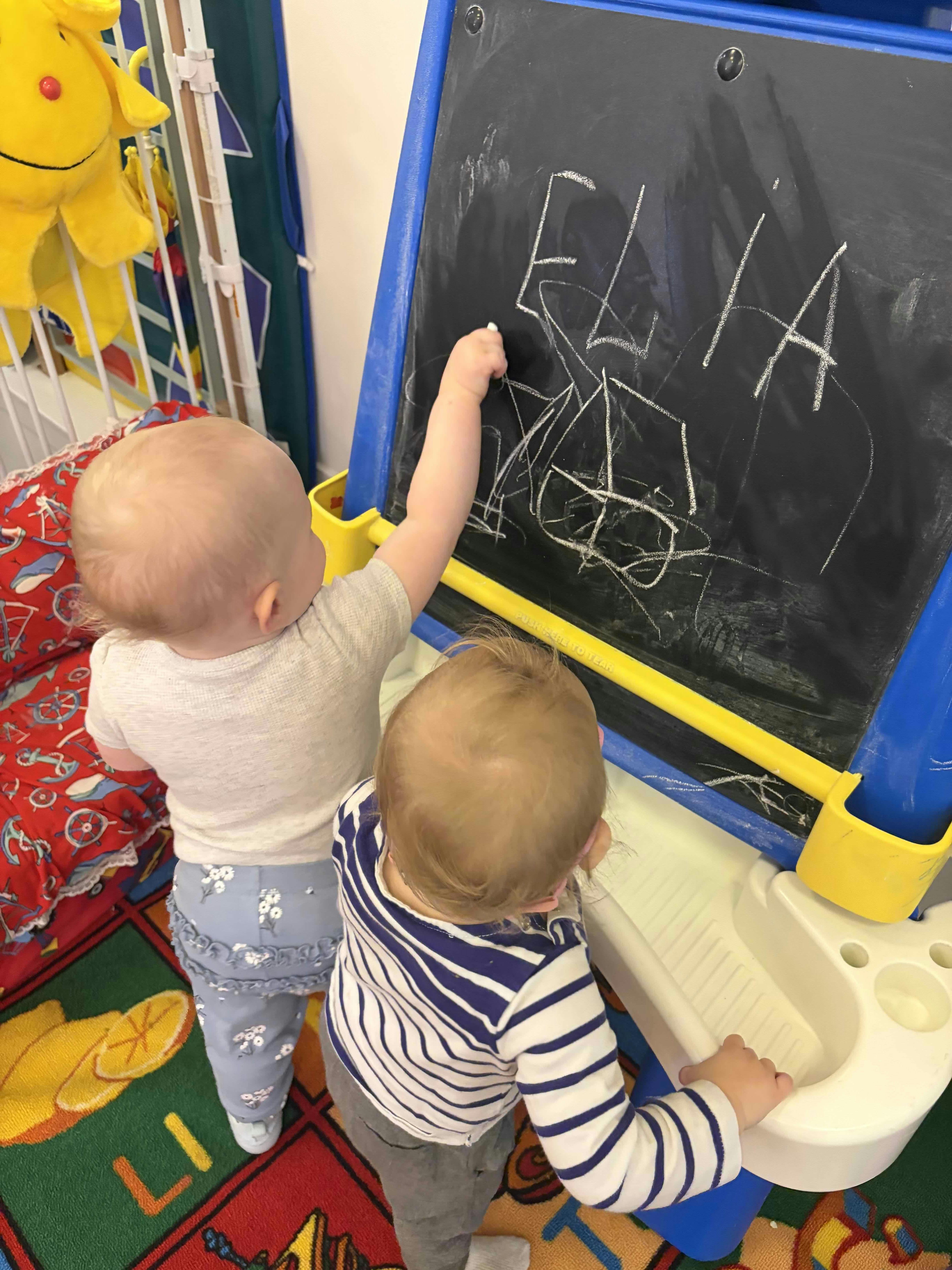 Two children standing and drawing with chalk on a small blackboard