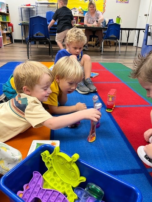 Children playing with toys on a colorful mat in a classroom