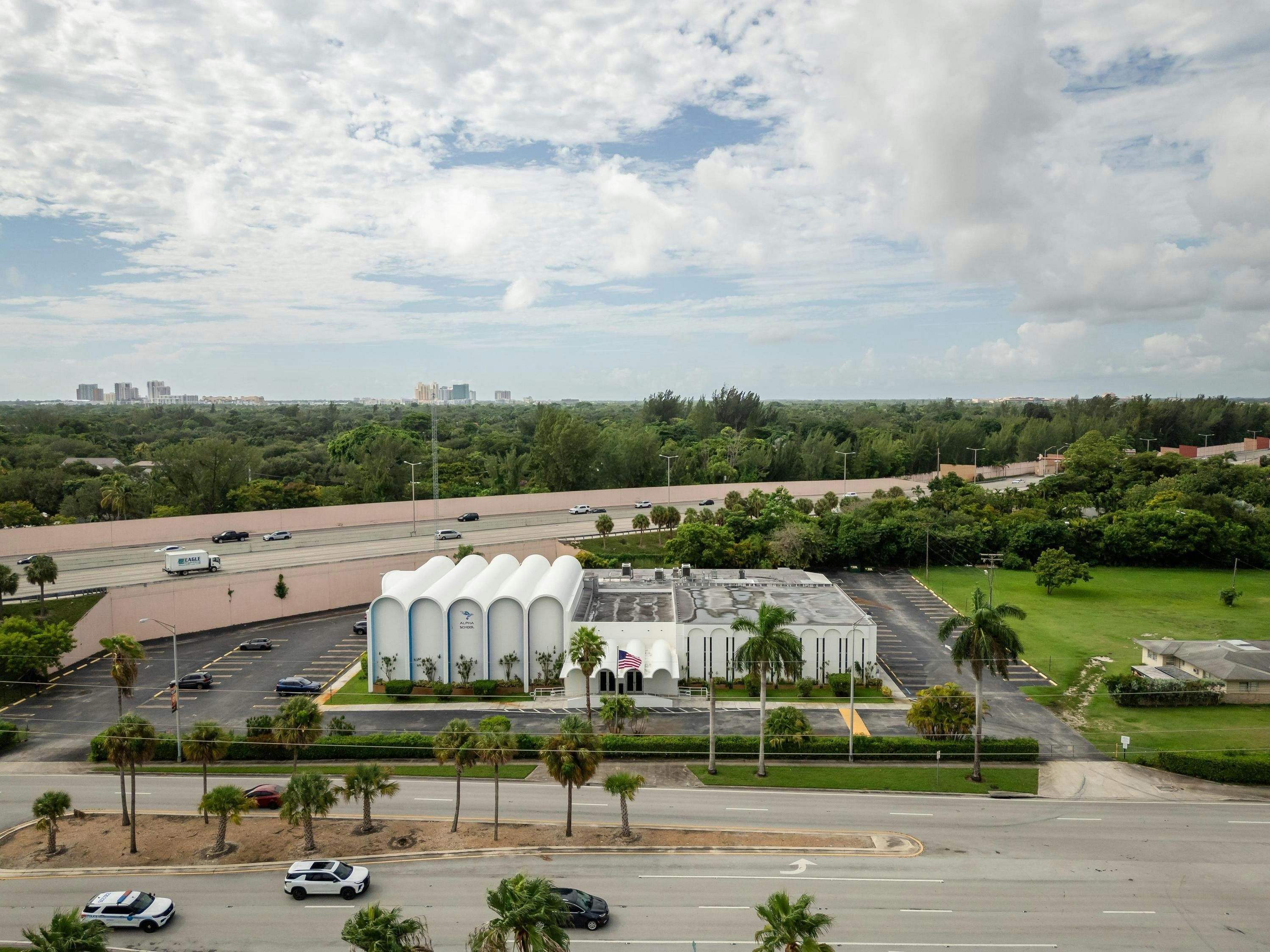 Aerial view of a white building with "Alpha School" on it, near a highway