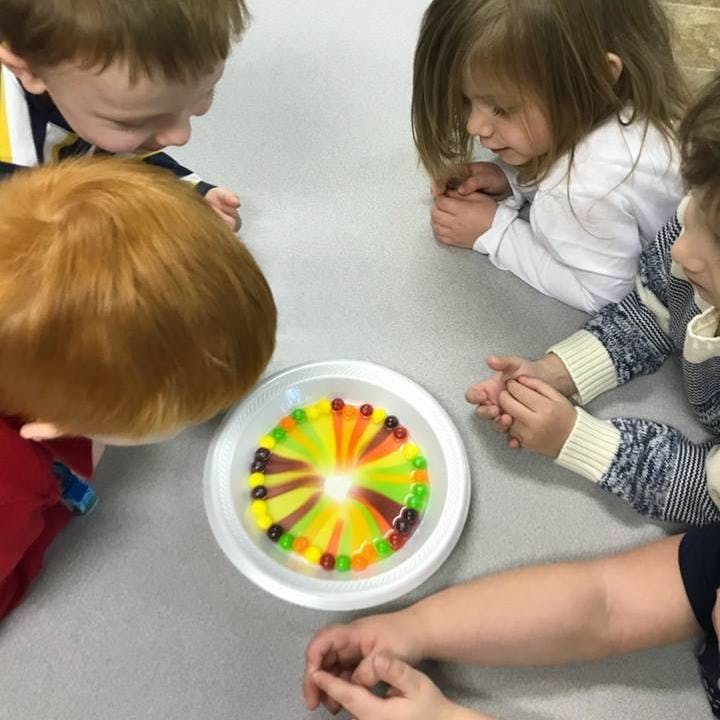 Children looking at colorful candies dissolving in a plate of liquid